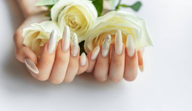 Beyaz bir zemin üzerinde kadın elleri Güzel bir inci manikür ve beyaz gül