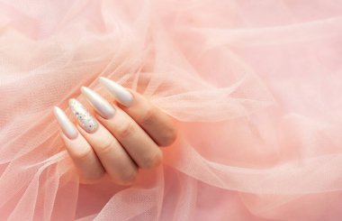 Pembe arka planda güzel inci manikürlü kadın elleri.