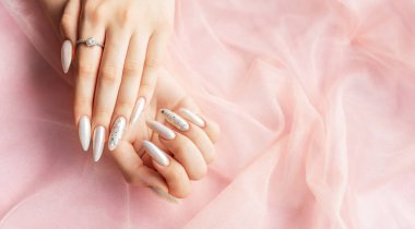 Pembe arka planda güzel inci manikürlü kadın elleri.