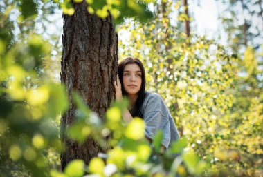 Genç bir kız ormanda bir ağaca sarılıyor. Stresi azaltmak ve doğayla bağ kurmak için ağaçlara sarılıp dokunmak..