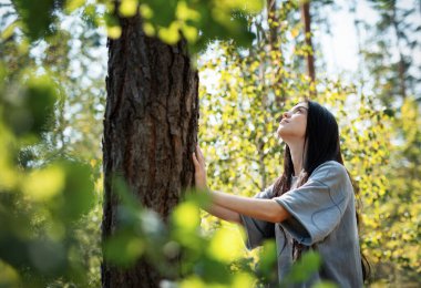 Genç bir kız ormanda bir ağaca sarılıyor. Stresi azaltmak ve doğayla bağ kurmak için ağaçlara sarılıp dokunmak..