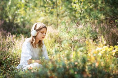 Girl listening to music with headphones. Young teenage girl in the forest clipart