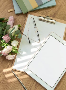 Parlak bir çalışma alanı, boş bir tablet, açık bir defter, kırtasiye araçları ve ahşap bir masaya dizilmiş taze çiçekler, yaratıcılığı ve planlamayı davet eder..
