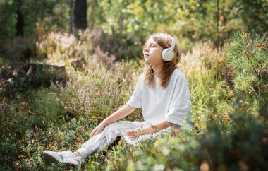 Kulaklıkla müzik dinleyen bir kız. Ormandaki genç kız