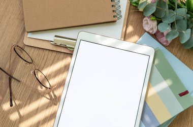 Çalışma alanı bir tablet, gözlük, kırtasiye ve yeşil yapraklar ile düzenlenmiştir, hepsi odaklanmak ve yaratıcılık için sakin bir atmosfer oluşturmak için uyum içinde düzenlenmiştir..