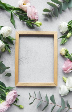 Yumuşak çiçekler, açık gri bir yüzey üzerinde dinlenen basit bir ahşap çerçeveyi sarar ve davetkar bir alan yaratır.