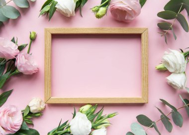 Ahşap bir çerçeve, yeşil okaliptüs yapraklarıyla birlikte yumuşak pembe ve beyaz güllerle çevrilidir ve çeşitli durumlar için uygun taze ve zarif bir dekoratif düzenleme oluşturur..