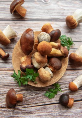 Değişik taze mantarlar ahşap bir tabakta sanatsal olarak sergilenir. Mutfak ortamında yeşil otlarla çevrili..