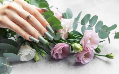 Uzun yeşil tırnaklı bir el, yumuşak ve huzurlu bir ortamda yemyeşil okaliptüs yapraklarıyla tamamlanmış pembe ve beyaz çiçeklerin güzel bir düzeninin yanında dinlenir..