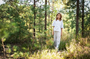 Küçük bir çocuk orman yolunda sessizce yürür, güneşin sıcaklığının ve etrafındaki ağaçların ve bitkilerin huzurunun tadını çıkararak, bir merak duygusunu somutlaştırır..