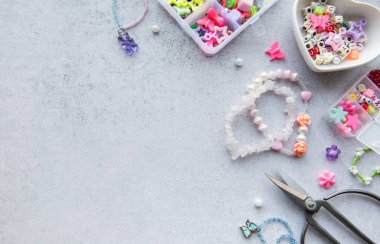 Boncuk işçiliği, gri bir yüzeye yayılmış çeşitli renkli boncuk ve aletler gösteriyor. Öğleden sonra ışığı altında eşsiz mücevherler yapmak için mükemmel..
