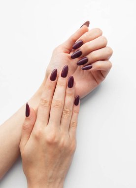 Son zamanlarda yapılan bir manikür seansının detaylarını vurgulayan, katıksız beyaz bir yüzeyde iki el şık bir bordo çivi tasarımı sergiliyor..