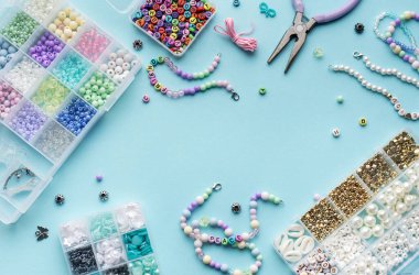 Yumuşak mavi arkaplan üzerindeki boncuklar, aletler ve bitmiş bileziklerden oluşan canlı bir düzenleme çeşitli renk ve tasarımlarla mücevher yapma sanatını gözler önüne seriyor..