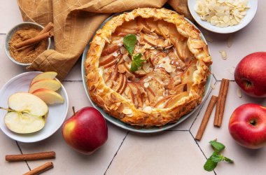 Yeni pişmiş bir elma galeti, kıtır elma dilimleri, badem taneleri ve bir tutam tarçın ile sergilenerek sıcak, davetkar bir atmosfer yaratılır..