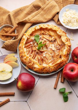 Yeni pişmiş bir elma galeti, kıtır elma dilimleri, badem taneleri ve bir tutam tarçın ile sergilenerek sıcak, davetkar bir atmosfer yaratılır..