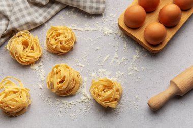 Tagliatelle, gri arka plana yerleştirilmiş un, yumurta ve oklavalı yuvaları menü veya yemek tarifi kitabı için güzel bir arka plan oluşturur.