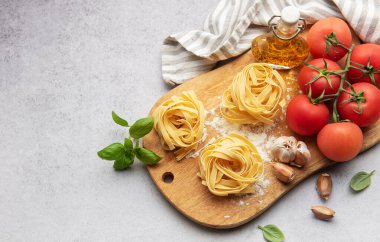 Tahta kesim tahtası, domates, sarımsak, fesleğen ve zeytinyağı üzerine pişmemiş tagliatelle makarna, İtalyan yemeği kavramı.