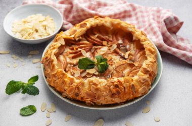 Açık yüzlü elma turtası, badem gevreği ve açık arkaplanda taze nane şekeri ile süslenmiş.