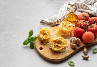 Tahta kesim tahtası, domates, sarımsak, fesleğen ve zeytinyağı üzerine pişmemiş tagliatelle makarna, İtalyan yemeği kavramı.