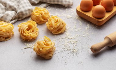 Tagliatelle, gri arka plana yerleştirilmiş un, yumurta ve oklavalı yuvaları menü veya yemek tarifi kitabı için güzel bir arka plan oluşturur.