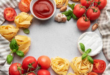 Domates, makarna, sarımsak, peynir, fesleğen ve domates soslu İtalyan yemekleri gri arka planda bir çerçeve oluşturur.