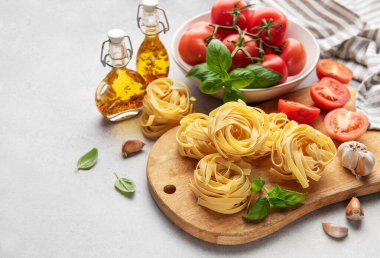 Tagliatelle makarna yuvaları, taze domatesler, fesleğen yaprakları ve baharatlı zeytinyağı mutfak masasında pişirilmeye hazır.