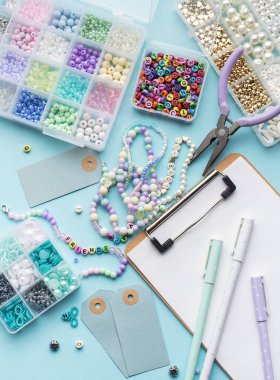 Mavi yüzeyde renkli boncuklar, pense, pano, fiyat etiketleri ve diğer araçlardan oluşan bilezikler yapmak için diy takımı