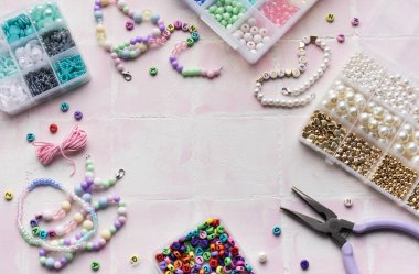 Renkli boncuklar, harf boncukları, ip, pense ve pense içeren el işi malzemeler pembe bir fayans yüzeyinde, mücevher yapımına hazır.