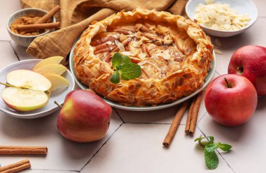 Yeni pişmiş bir elma galeti, kıtır elma dilimleri, badem taneleri ve bir tutam tarçın ile sergilenerek sıcak, davetkar bir atmosfer yaratılır..