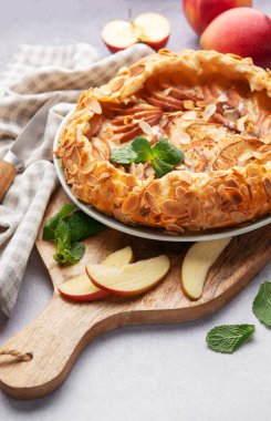 Badem gevreği ve nane ile süslenmiş taze pişmiş elma galetesi, taze elmalar ve bir bıçakla servis edilen bir masada.