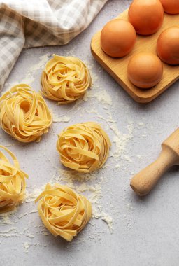 Tagliatelle, gri arka plana yerleştirilmiş un, yumurta ve oklavalı yuvaları menü veya yemek tarifi kitabı için güzel bir arka plan oluşturur.