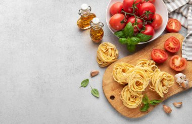 Tahta tahtada taze tagliatelle makarna. Etrafı olgun domatesler, sarımsak karanfilleri ve fesleğen yapraklarıyla çevrili. İtalyan mutfağı sahnesi hazırlıyorlar.