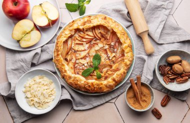 Badem gevreği, tarçın ve nane yapraklarıyla süslenmiş taze pişmiş elma galetesi.