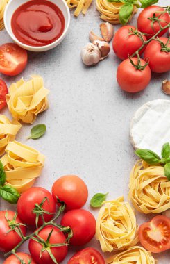 Domates, makarna, sarımsak, peynir, fesleğen ve domates soslu İtalyan yemekleri gri arka planda bir çerçeve oluşturur.