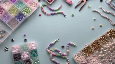 Kişi açık mavi arkaplanda renkli boncuklarla arkadaşlık bilezikleri yapıyor.