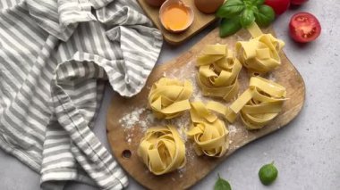 Şef, domates, yumurta ve fesleğen gibi malzemelerle çevrili ahşap bir tahtada taze tagliatelle makarnası hazırlıyor.