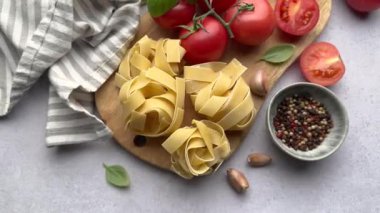Şef, domates, yumurta ve fesleğen gibi malzemelerle çevrili ahşap bir tahtada taze tagliatelle makarnası hazırlıyor.