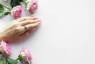 Zarif pembe manikürlü, gümüş yüzüklü ve beyaz arka planda pembe güllü bir kadın.