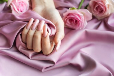 Pembe manikürlü bir kadın pembe ipek arka planda pembe bir gül tutuyor.