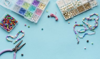 Yumuşak mavi arkaplan üzerindeki boncuklar, aletler ve bitmiş bileziklerden oluşan canlı bir düzenleme çeşitli renk ve tasarımlarla mücevher yapma sanatını gözler önüne seriyor..