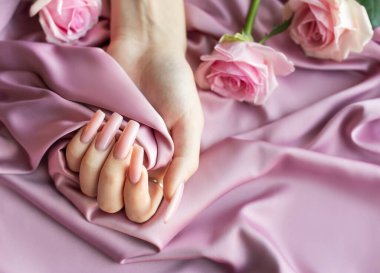 Pembe manikürlü bir kadın pembe ipek arka planda pembe bir gül tutuyor.