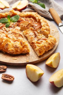 Badem taneleri ve nane yapraklarıyla süslenmiş taze pişmiş elma galetesi ahşap bir tahtada servis edilir.