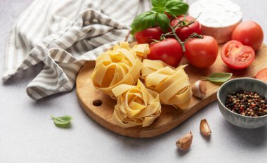 İtalyan makarna tagliatelle yuvaları domates, sarımsak, peynir ve fesleğen ahşap kesim tahtasının üzerinde dinleniyor.