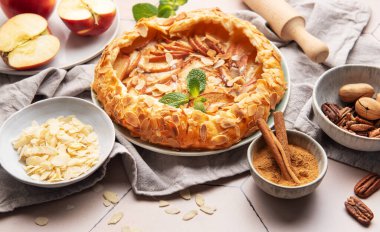 Badem taneli, tarçınlı ve naneli taze pişmiş elma galetesi. Etrafı malzemelerle ve mutfak malzemeleriyle çevrili.