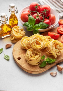 Tagliatelle makarna yuvaları, taze domatesler, fesleğen yaprakları ve baharatlı zeytinyağı mutfak masasında pişirilmeye hazır.