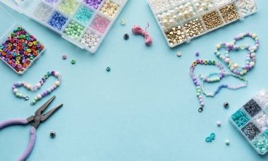 Yumuşak mavi arkaplan üzerindeki boncuklar, aletler ve bitmiş bileziklerden oluşan canlı bir düzenleme çeşitli renk ve tasarımlarla mücevher yapma sanatını gözler önüne seriyor..