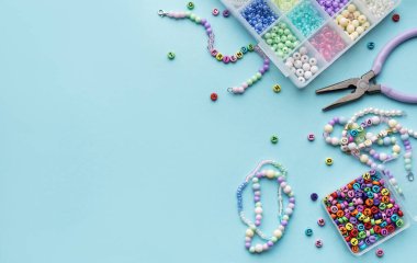 Yumuşak mavi arkaplan üzerindeki boncuklar, aletler ve bitmiş bileziklerden oluşan canlı bir düzenleme çeşitli renk ve tasarımlarla mücevher yapma sanatını gözler önüne seriyor..