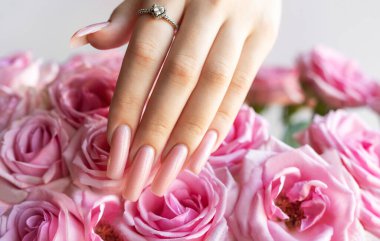 Pembe manikürlü ve pırlanta yüzüklü narin kadın eli nazikçe pembe gül buketine dokunuyor.