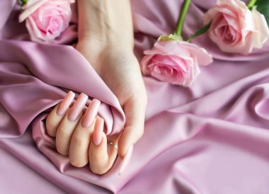 Pembe manikürlü bir kadın pembe ipek arka planda pembe bir gül tutuyor.