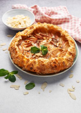 Açık yüzlü elma turtası, badem gevreği ve açık arkaplanda taze nane şekeri ile süslenmiş.